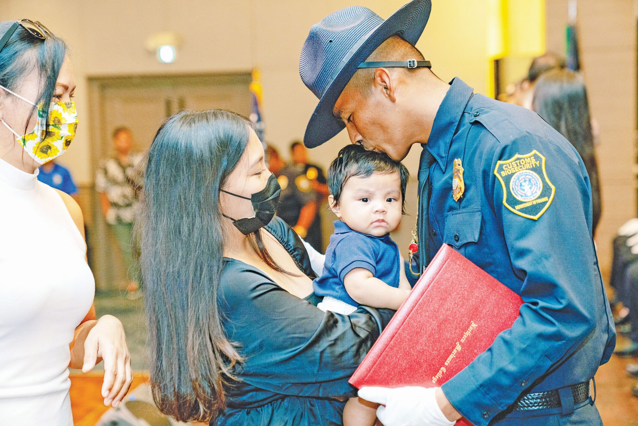 Customs and Biosecurity graduate Kane P. Ybanez plants a kiss on his son’s head after receiving his badge during the Division of Customs and Biosecurity 9th Cycle Academy graduation yesterday, July 25, 2022, at the Saipan World Resort’s Royal Taga Ballroom. The academy was coordinated in partnership with Northern Marianas College. Ybanez, who received a leadership recognition award during the ceremony, joins 28 other Customs and Biosecurity graduates. (NMC)