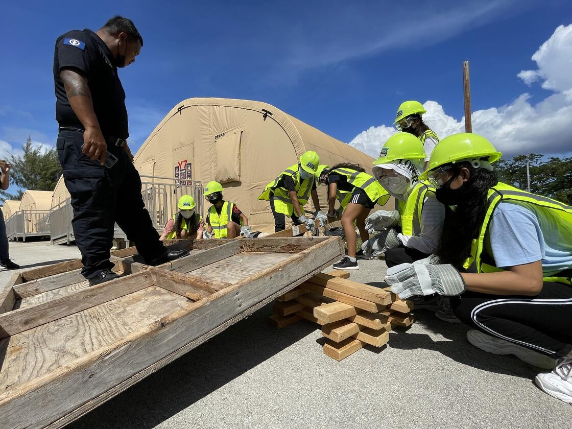 Department of Fire and Emergency Medical Services Firefighter III Patrick George conducts a "cribbing" simulation activity with members of NMC’s My Preparedness Initiative (MyPI). The members are being timed and challenged to see how fast they can remove a victim from under the structure.